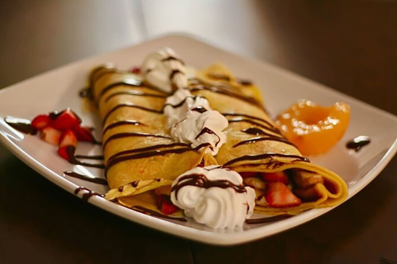 Een bord pannenkoeken met slagroom en siroop, versierd met aardbeien en een perzik.