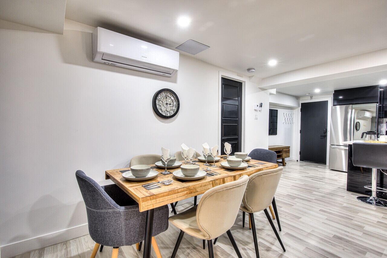 Een moderne eetruimte met een houten tafel voor vier personen, omringd door stoelen. Een airconditioner is aan de muur boven de tafel bevestigd.