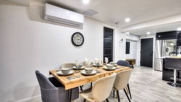 Een moderne eetruimte met een houten tafel voor vier personen, omringd door stoelen. Een airconditioner is aan de muur boven de tafel bevestigd.