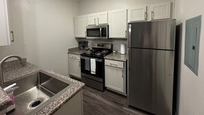 A modern kitchen with stainless steel appliances, white cabinets, and a granite countertop. - LuxeWoodlands Villa: Cozy Stay (Conroe)