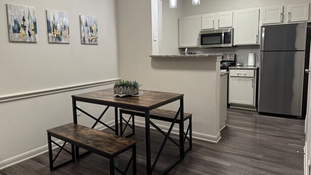 A modern kitchen with white cabinets, stainless steel appliances, and a dark wood dining table with benches. - LuxeWoodlands Villa: Cozy Stay (Conroe)
