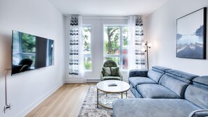 Moderni olohuone, jossa on litteänäyttöinen televisio, sininen sohva, vihreä nojatuoli ja pyöreä sohvapöytä.