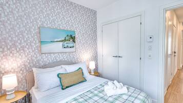 Ein ordentlich eingerichtetes Schlafzimmer mit Bett, Kissen, einer Nachttischlampe, einem Bild mit Strandmotiv und einem Kleiderschrank.
