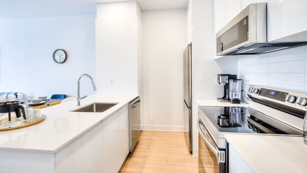 Una cocina moderna con armarios blancos, un refrigerador de acero inoxidable, horno empotrado y cafetera.