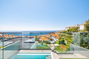 A modern rooftop pool with glass railings, a clear view of the sea, and terraced buildings in the background. - Art House - By WeHostMadeira (Funchal)