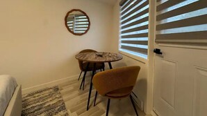 Um quarto pequeno com uma cama, uma mesa redonda com duas cadeiras, um espelho na parede e uma porta com persianas.