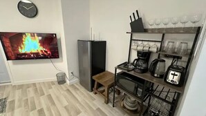 Cozinha compacta com TV, geladeira, cafeteira, torradeira e copos de vinho nas prateleiras.