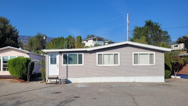 A single-story mobile home with a front porch, a small attached garage, and a clear view of the surrounding area. - $2,175 / 3br - 1450ft2 - 3 Beds 2 Baths House (Osoyoos) (Osoyoos)
