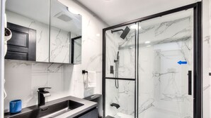 A modern bathroom with a glass-enclosed shower, a sink with a black faucet, and a marble-tiled wall. - NEW! NDG Studio for High Value Rest & Adventure (Montréal)