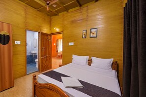 A wooden-paneled room with a bed, a wooden door, and a small bathroom visible through an open door. - Holidayz by Stayz Royale Yercaud (Yercaud)