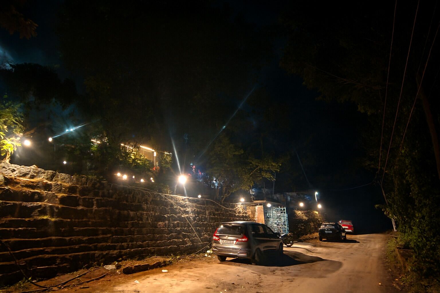 A nighttime scene of a rural road with a stone wall on one side and a parked car.