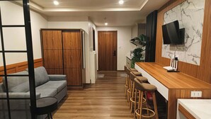 Un salon moderne comprenant un canapé, une table basse, un téléviseur fixé sur un mur en marbre et un coin repas en bois avec des tabourets de bar.