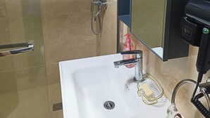 Une salle de bain avec une douche à parois de verre, un lavabo blanc, un miroir et un sèche-cheveux.
