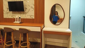 Une chambre d’hôtel avec un mur en marbre, un téléviseur à écran plat, une coiffeuse en bois et un miroir.