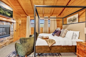 L'intérieur d'un chalet en bois, avec un lit, une cheminée en pierre et un fauteuil vert.