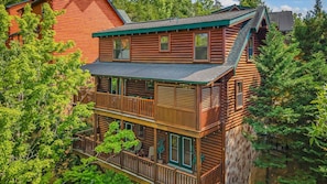 A multi-story log cabin with a balcony, surrounded by trees. - Luxury 5BR Cabin • Game Room • Hot Tub • Kids Loft • 10min to Dollywood (Pigeon Forge)