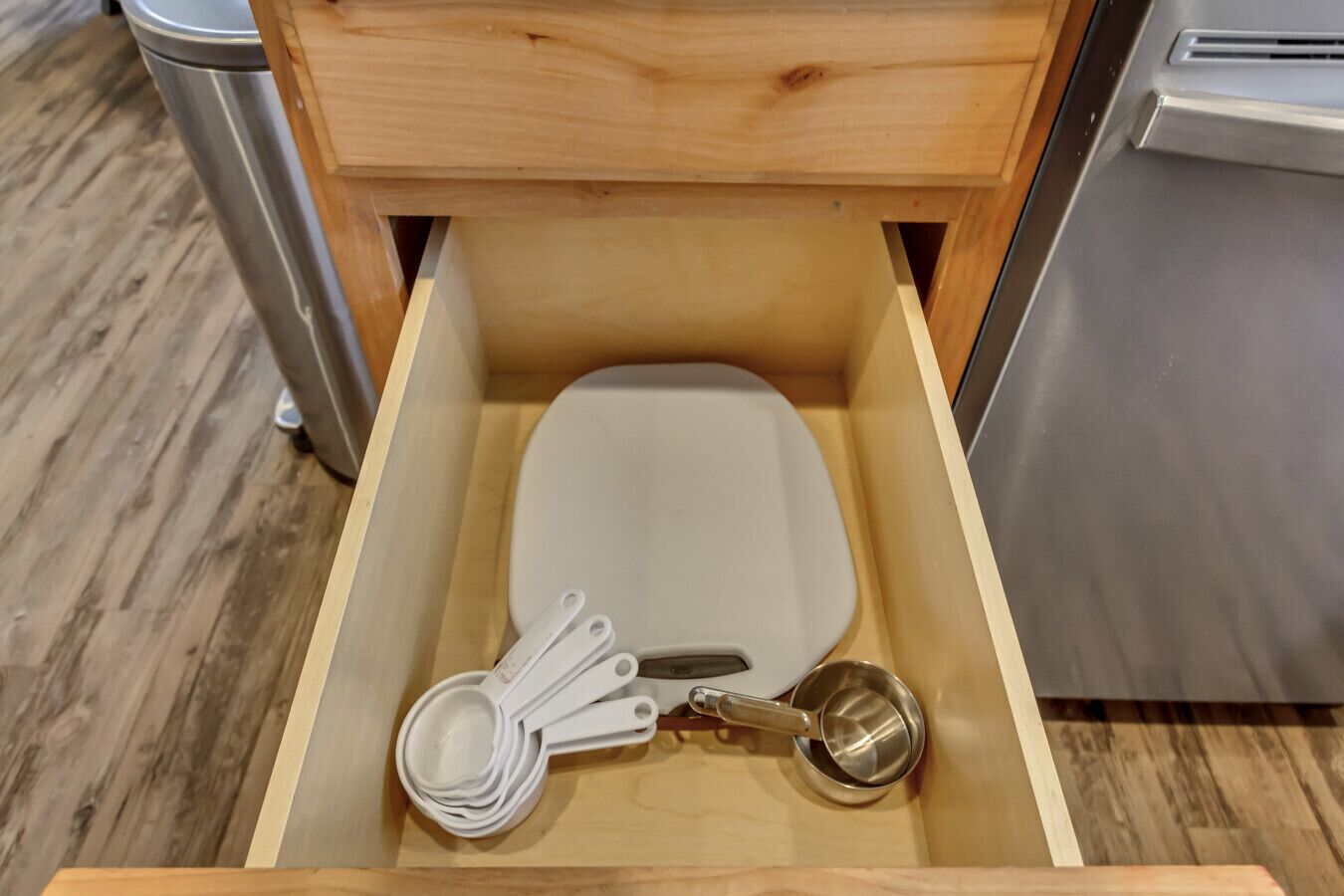 Un cajón de cocina con un bol blanco, cucharas medidoras y un colador de metal.