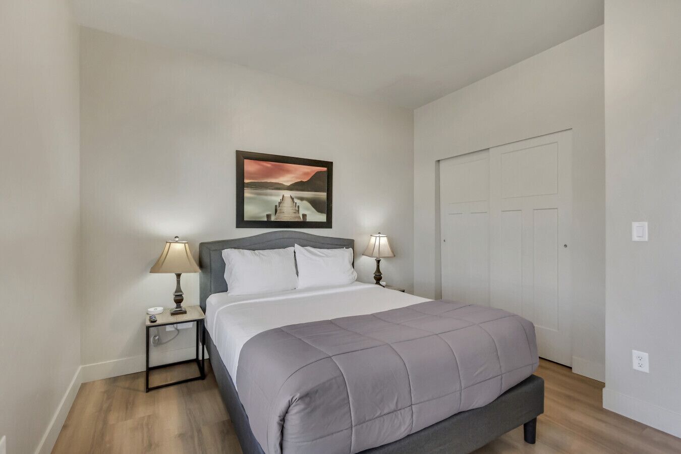 A bedroom with a bed, two bedside tables with lamps, a wall-mounted picture, and a door.