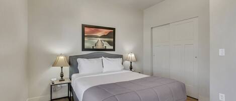 A bedroom with a bed, two bedside tables with lamps, a wall-mounted picture, and a door.