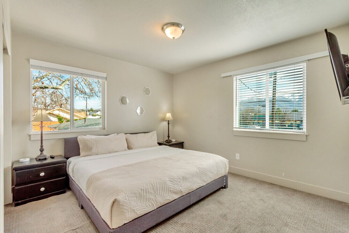 A bedroom with a bed, nightstands, a lamp, and two windows.
