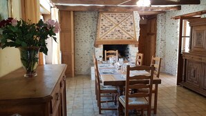 Ein Essbereich mit einem Holztisch, gedeckt für sechs Personen, mit Stühlen an beiden Seiten, in einem Raum mit freiliegenden Backsteinwänden und Kamin.