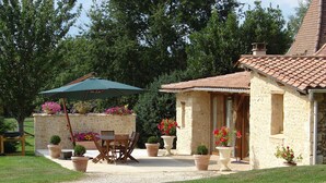 Ein Haus aus Stein mit einem Ziegeldach, einer Terrasse mit Tisch und Stühlen sowie Topfpflanzen.