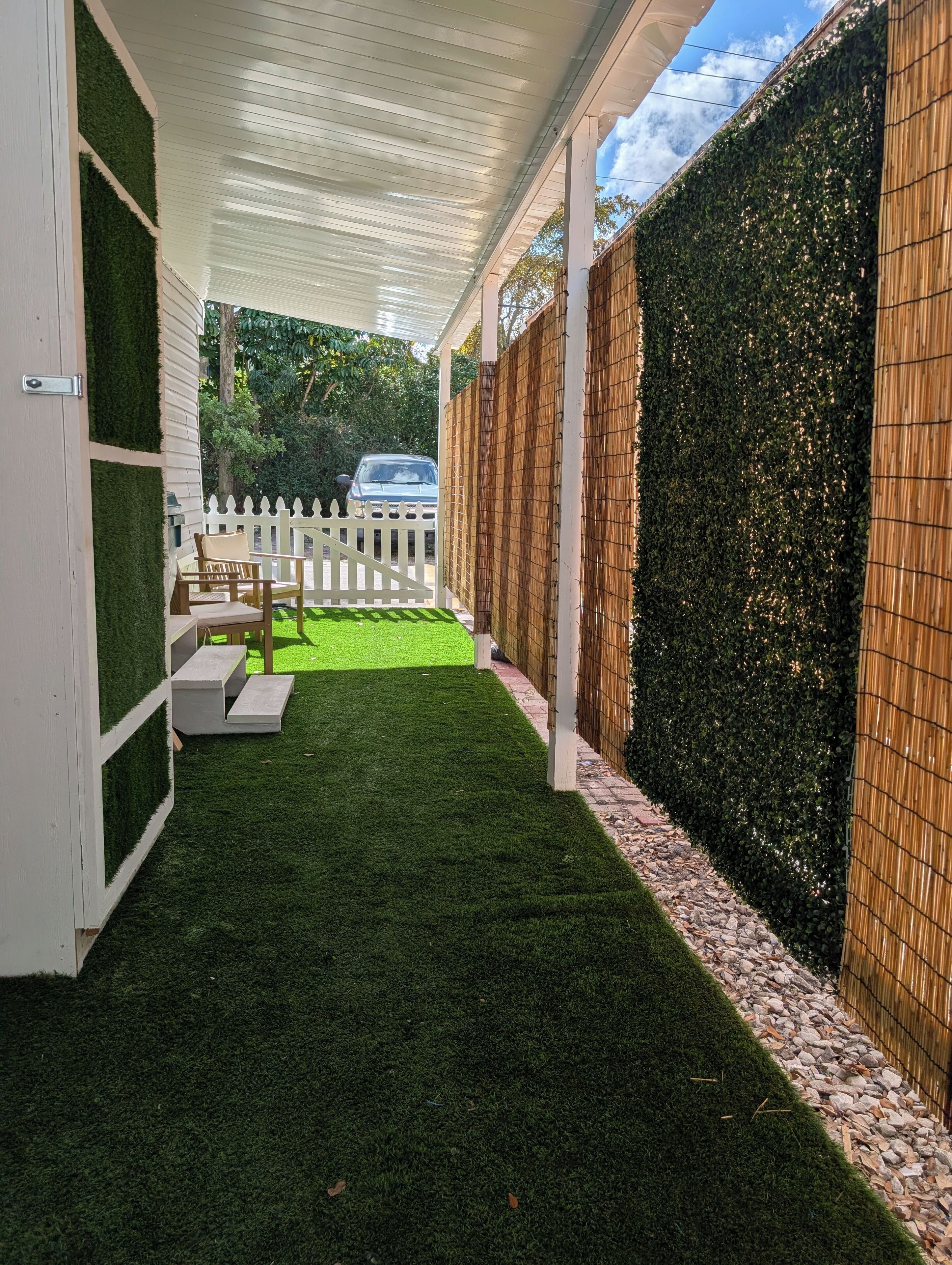 Un patio cubierto con césped artificial, cerca blanca y pared de bambú.