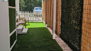 Un patio cubierto con césped artificial, cerca blanca y pared de bambú.
