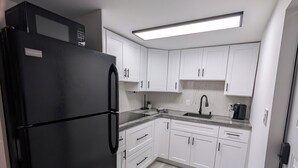 Una cocina moderna con armarios blancos, un refrigerador negro, una encimera de granito y un microondas integrado.
