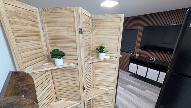 Una cocina moderna con un separador de madera, estantes empotrados, un televisor de pantalla plana y un refrigerador negro.