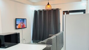 Una cocina compacta con microondas, una mesa blanca, un sofá gris y un refrigerador blanco.