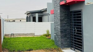 Un edificio moderno con fachada gris, un detalle rojo en la esquina superior derecha y una puerta metálica.