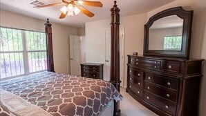Ein Schlafzimmer mit einem großen Bett, einem Schminktisch mit Spiegel, einem Deckenventilator und einem Fenster mit Blick auf Bäume.
