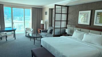 A hotel room with a large bed, a desk, a chair, a small table, and a view of the city.