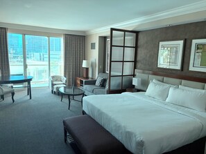 Ein Hotelzimmer mit einem großen Bett, einem Schreibtisch, einem Stuhl, einem kleinen Tisch und Blick auf die Stadt.