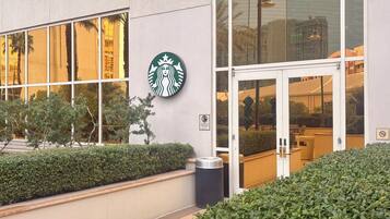 Ein Starbucks-Filiale mit großem Glasfassade, einer Klingel über der Tür und einem Schild, das einen Raucherbereich kennzeichnet.
