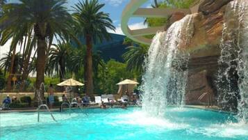 Ein Pool mit klarem, blauem Wasser, Palmen und einem Wasserfall.