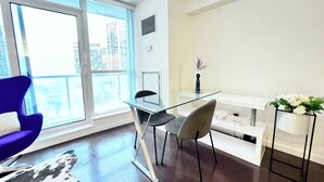 Ein modernes Wohnzimmer mit einem Glastisch, zwei Stühlen, einer Couch und einem großen Fenster mit Blick auf die Stadt.