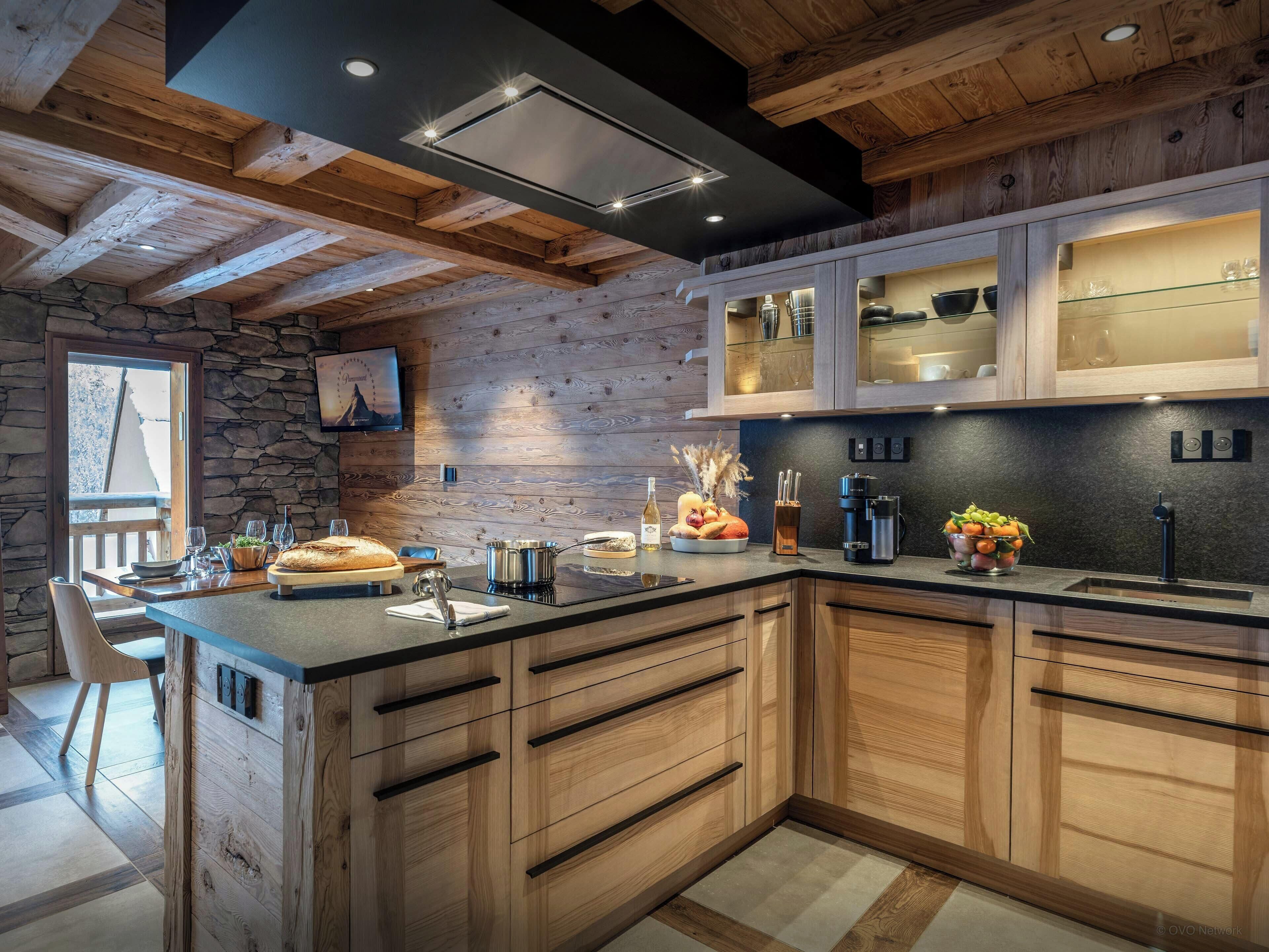 Une cuisine moderne avec des meubles en bois, un mur en pierre et un grand îlot central doté d’un évier et d’appareils électroménagers.