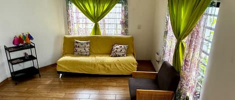 Una habitación con un sofá, una silla, una mesita y una estantería con objetos encima.