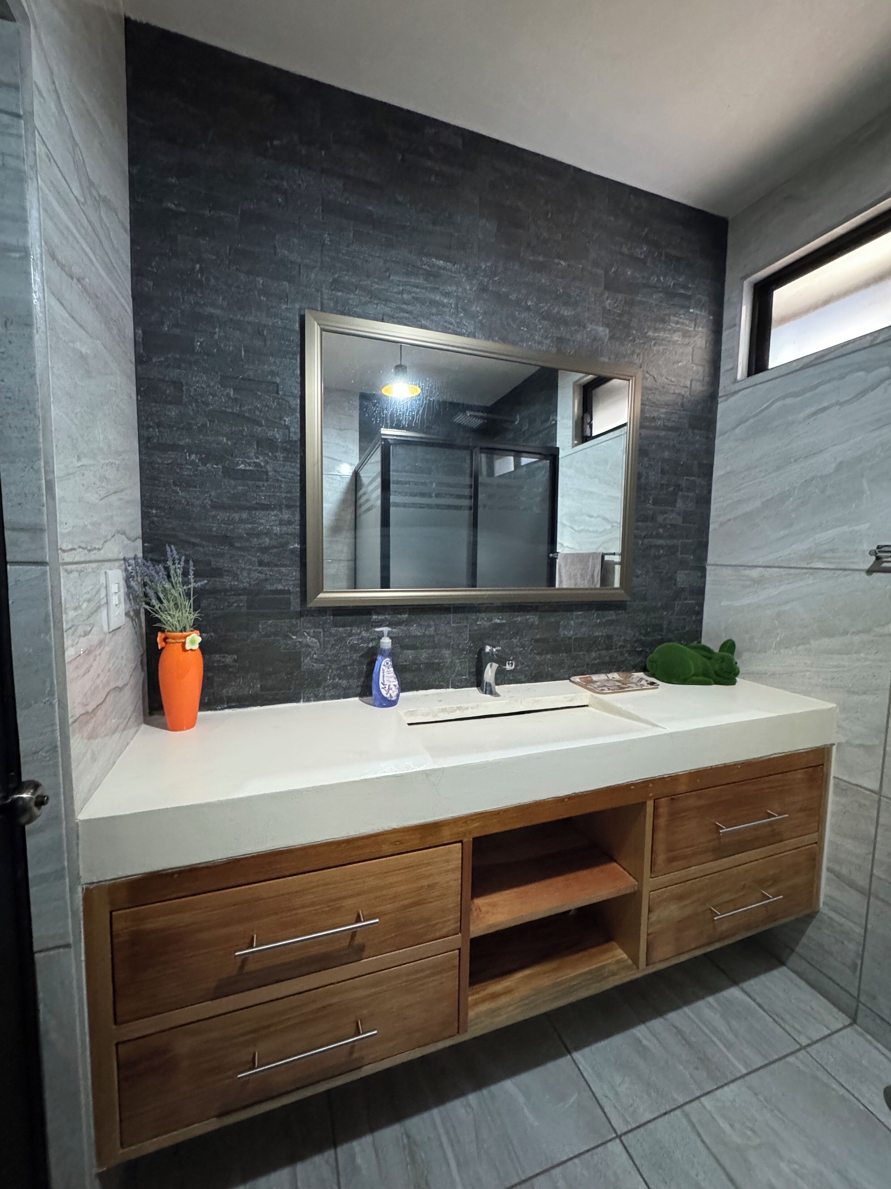 A bathroom with a modern vanity, a large mirror, and a potted plant.
