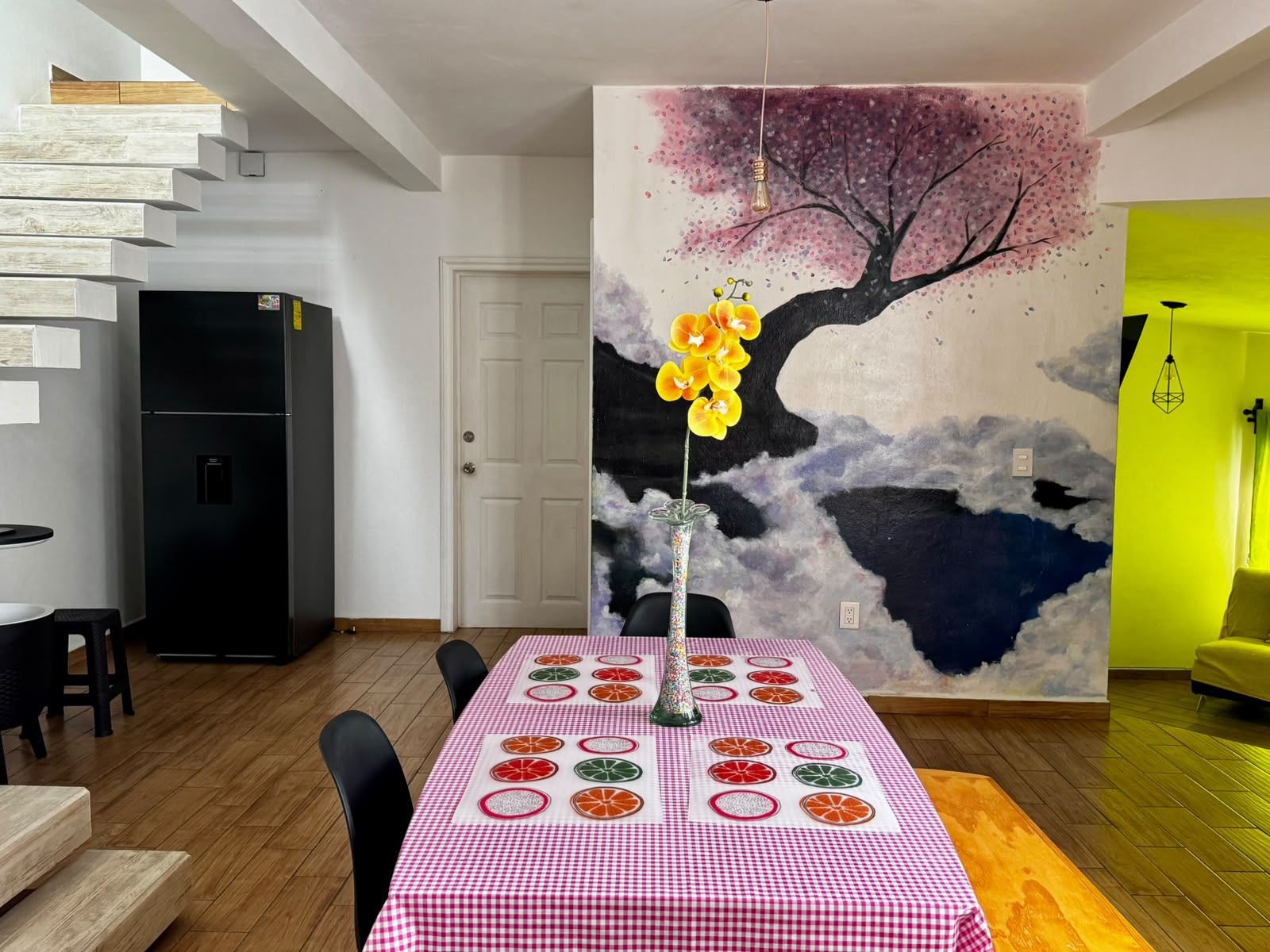 Un coin repas avec une nappe à carreaux, un vase rempli de fleurs et une fresque murale.