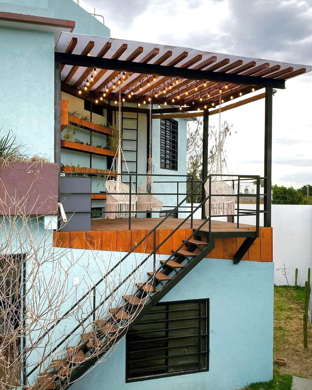 Una casa moderna con un espacio exterior techado, una escalera y una pérgola con luces colgantes.