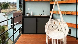 A balcony with a hanging macrame chair, a small kitchen area, and shelves with plants. - Casa Terraza Oaxaca (Oaxaca de Juárez)