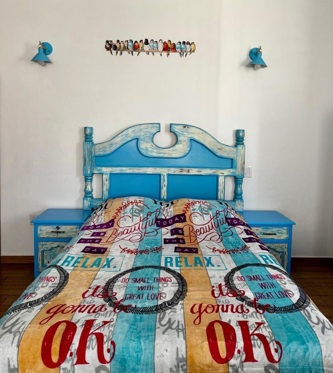 A bed with a blue headboard and a colorful bedspread with motivational phrases.