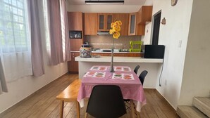 A dining area with a table set for two, wooden flooring, and a kitchen in the background. - Casa Terraza Oaxaca (Oaxaca de Juárez)