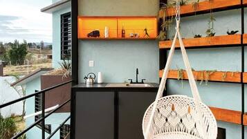 Ein Balkon mit einem hängenden Makramee-Stuhl, einer kleinen Küchenzeile und Regalen mit Pflanzen.