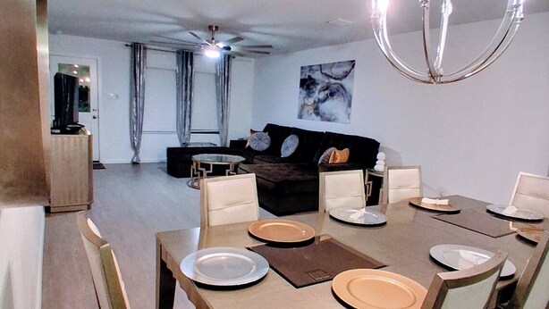 Un comedor con una mesa preparada para cuatro personas, un sofá al fondo y una araña colgante.