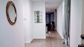 Un pasillo con piso de madera, un espejo redondo y un cuadro en la pared.