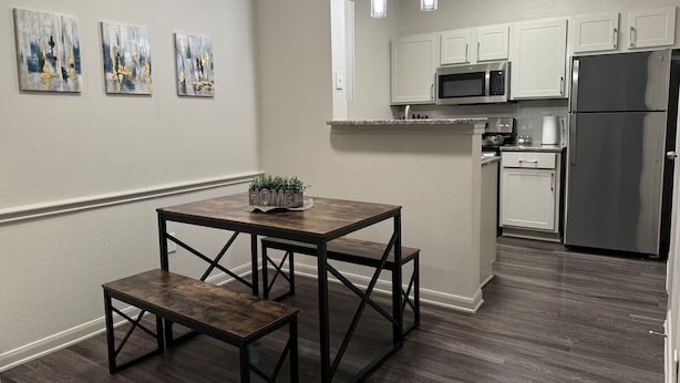 A modern kitchen with white cabinets, stainless steel appliances, and a dark wood dining table with benches. - Chic Apt in The Woodlands-Parking-WI-FI-King Bed (Conroe)